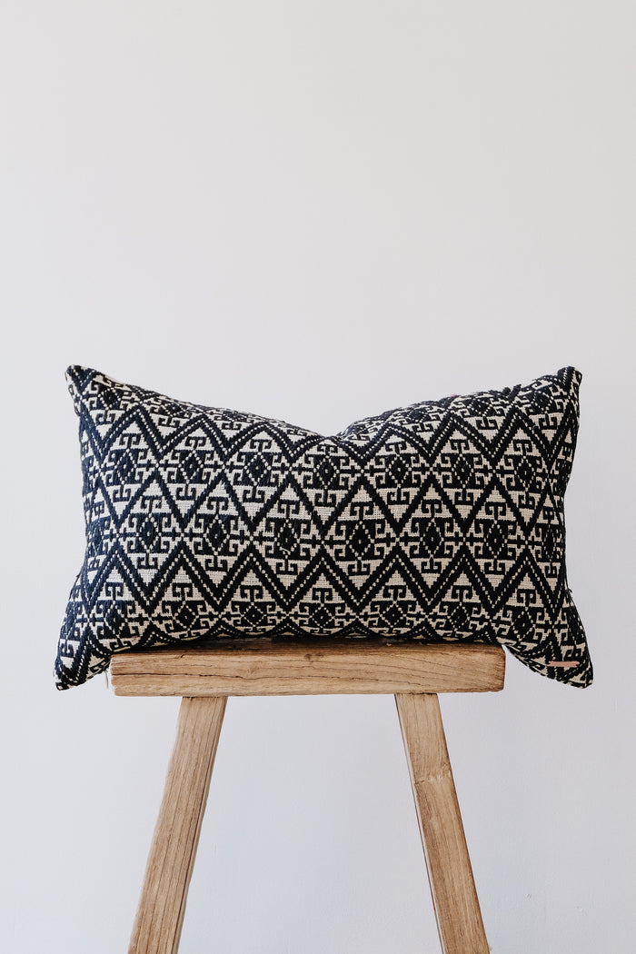 Front view of No. 24 - Antique Miao Lumbar Pillow on an Antique Stool against a white wall. - Saffron and Poe