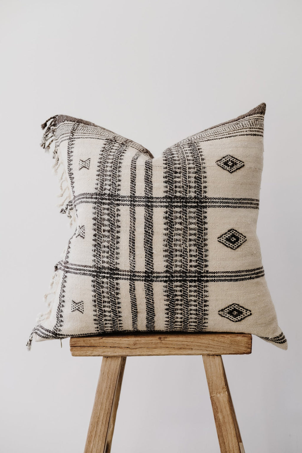 Handwoven Bhujodi pillow with black geometric patterns and tassels on wooden stool