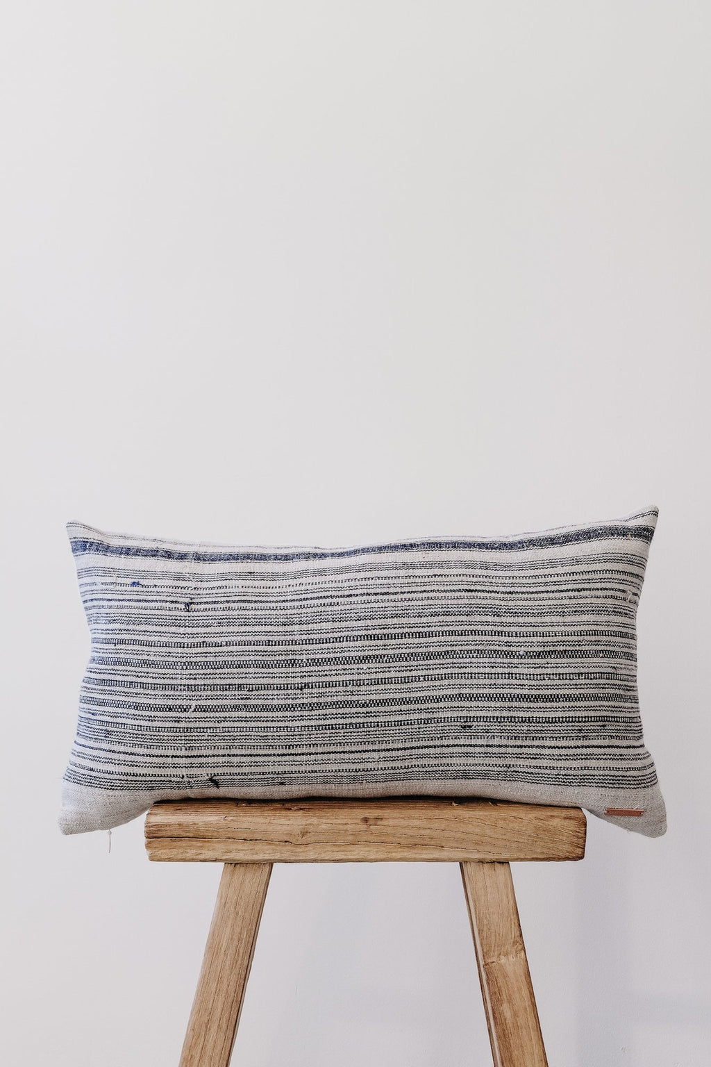 Vintage Hmong lumbar pillow with handwoven indigo stripes on wooden stool