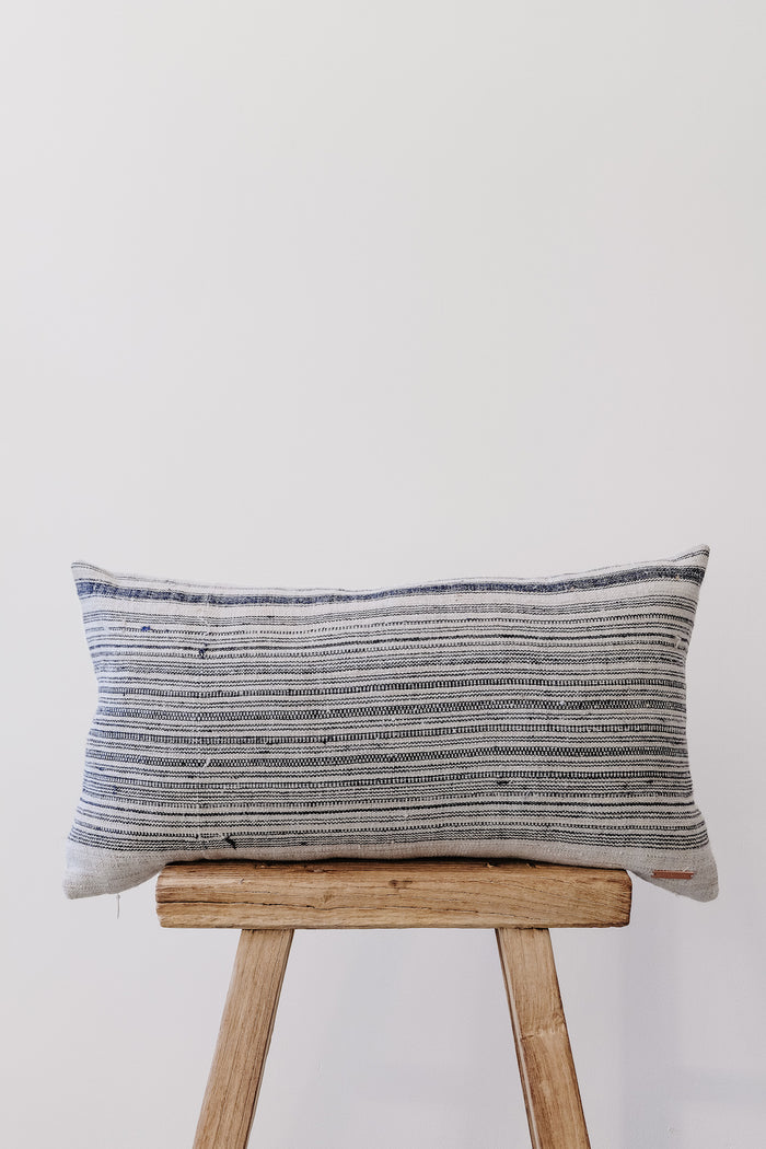 Front view of No. 35 - Hmong Hemp Lumbar PIllow on an Antique Stool against a white wall. - Saffron and Poe