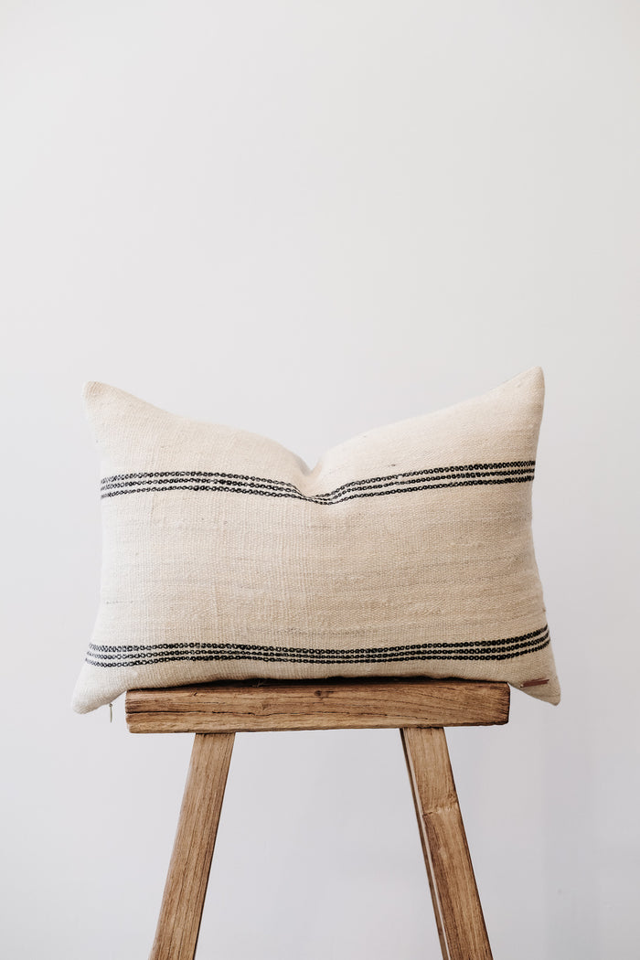 Front view of No. 37 - Handwoven Bhujodi Lumbar Pillow - Natural on an Antique Stool against a white wall. - Saffron and Poe