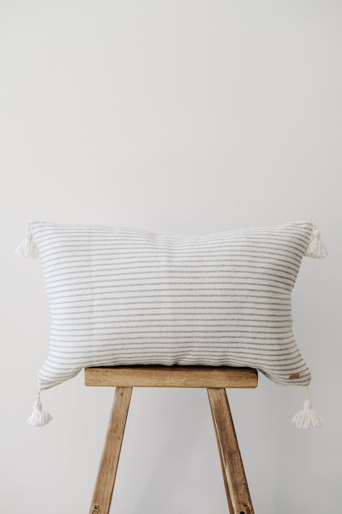 Front view of No. 37 - Moroccan Pom Pom Striped Pillow - Grey on a Chinese Stool against a white wall. - Saffron and Poe