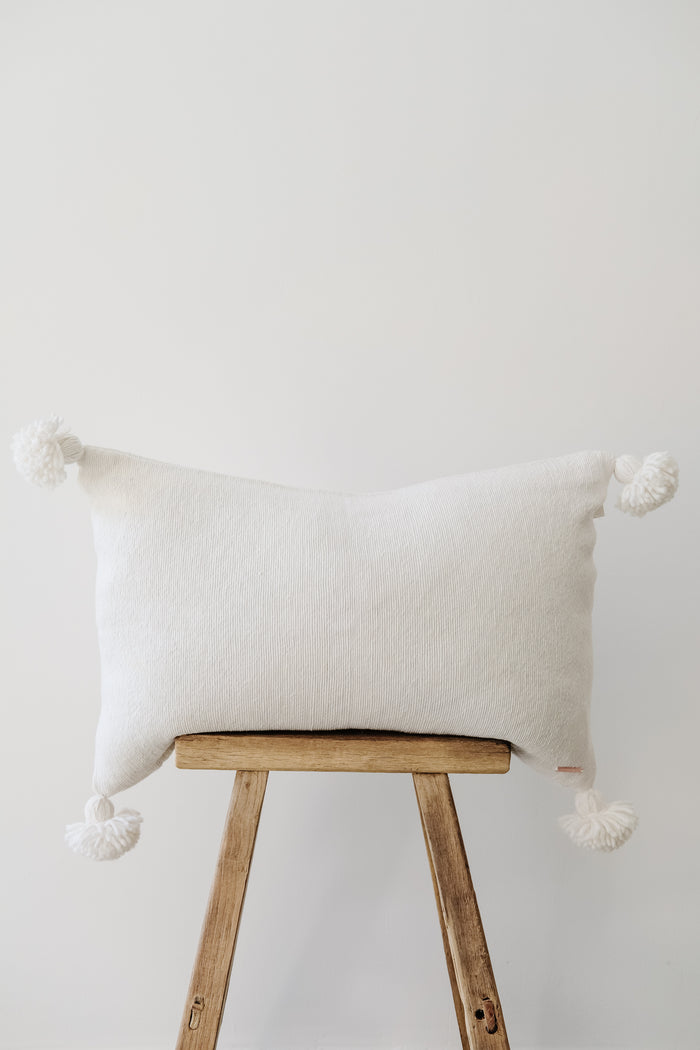 Front view of No. 38 - Moroccan Pom Pom Pillow - White on a Chinese Stool against a white wall. - Saffron and Poe