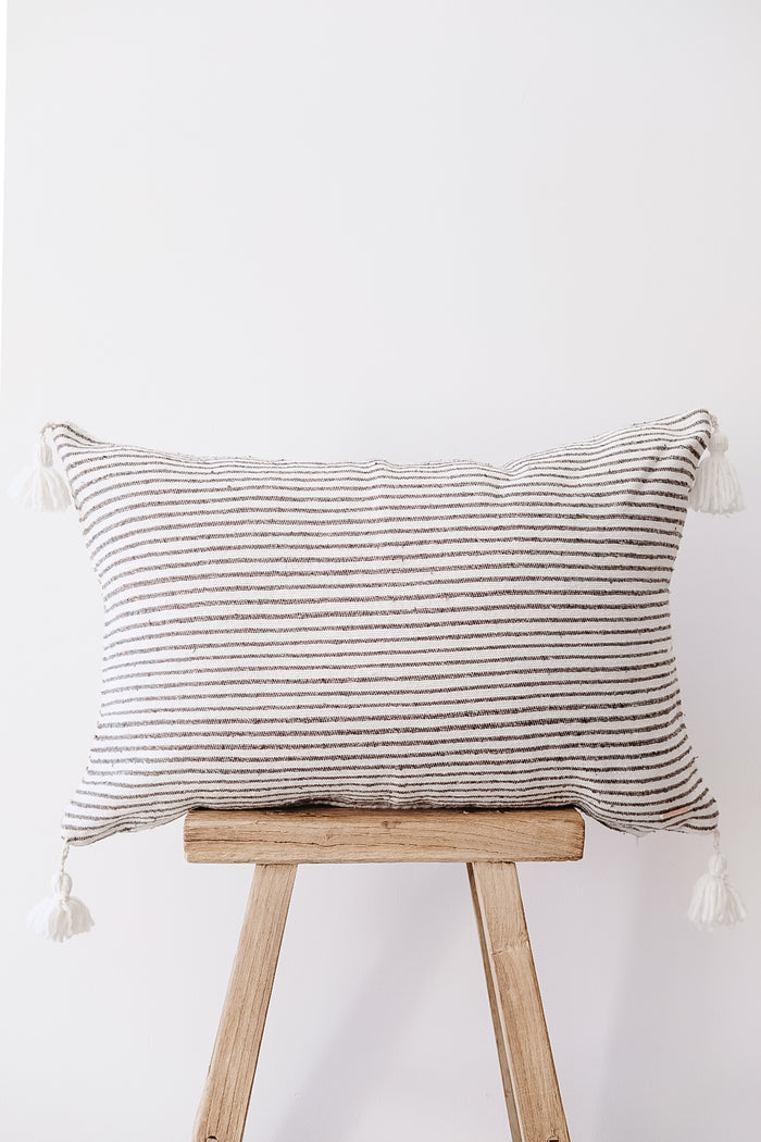 Front view of No. 40 - Moroccan Pom Pom Striped Pillow - Dark Grey on a Chinese Stool against a white wall. - Saffron and Poe