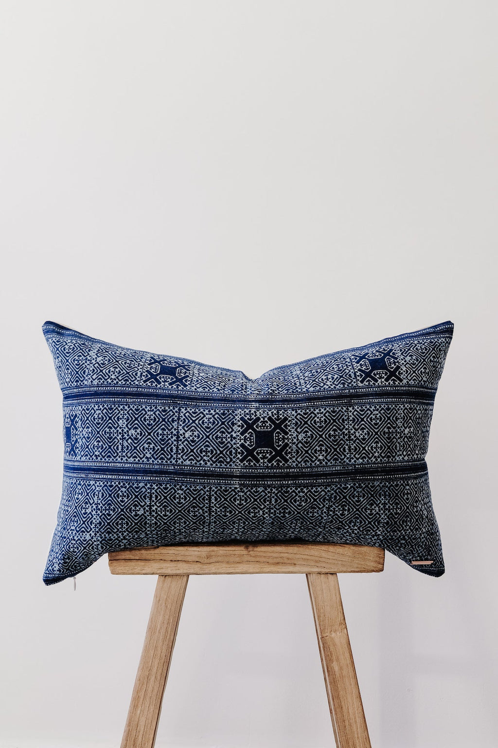 Hmong Batik lumbar pillow with intricate indigo blue patterns on wooden stool