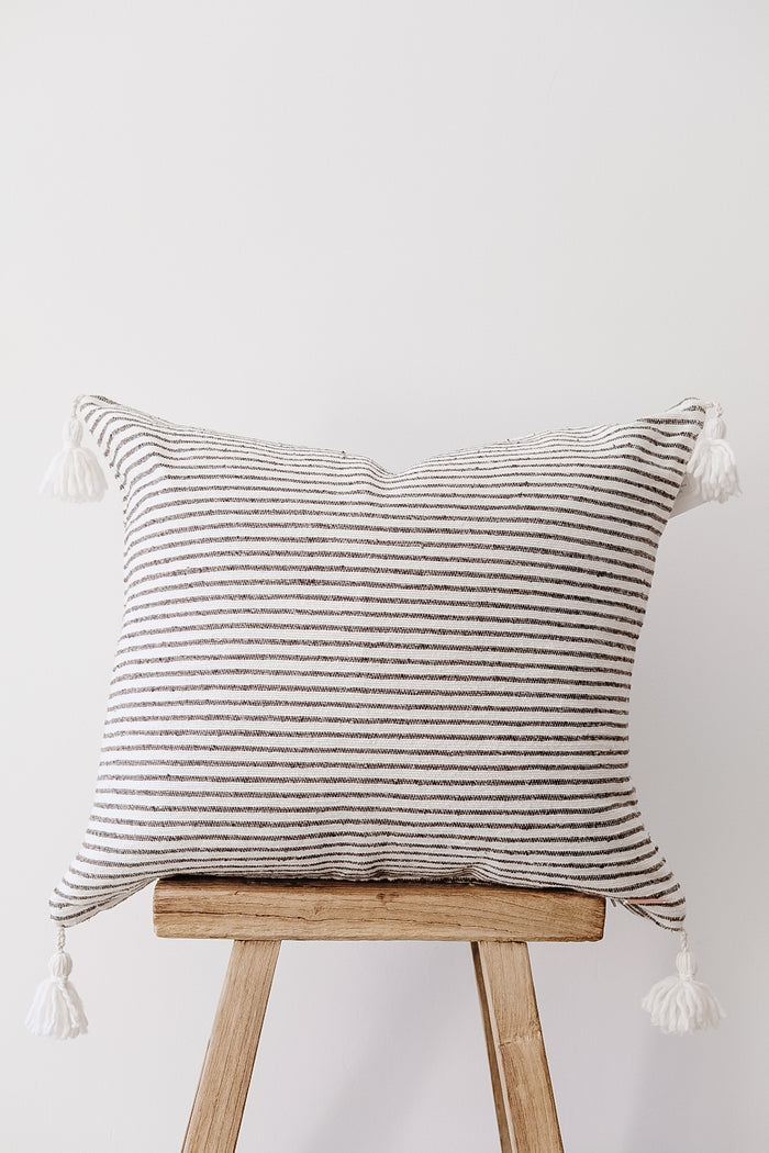 Front view of No. 41 - Moroccan Pom Pom Striped Pillow - Dark Grey on a Chinese Stool against a white wall. - Saffron and Poe