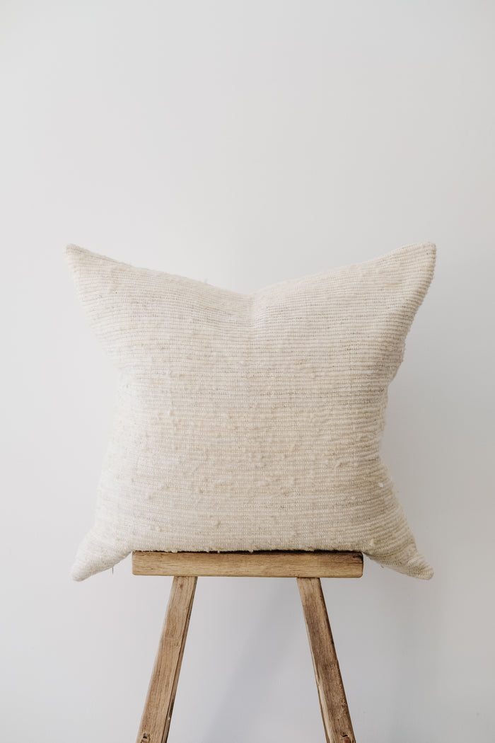 Front view of No. 47 - Ivory Handwoven Columbian Pillow on a Chinese Stool against a white wall. - Saffron and Poe