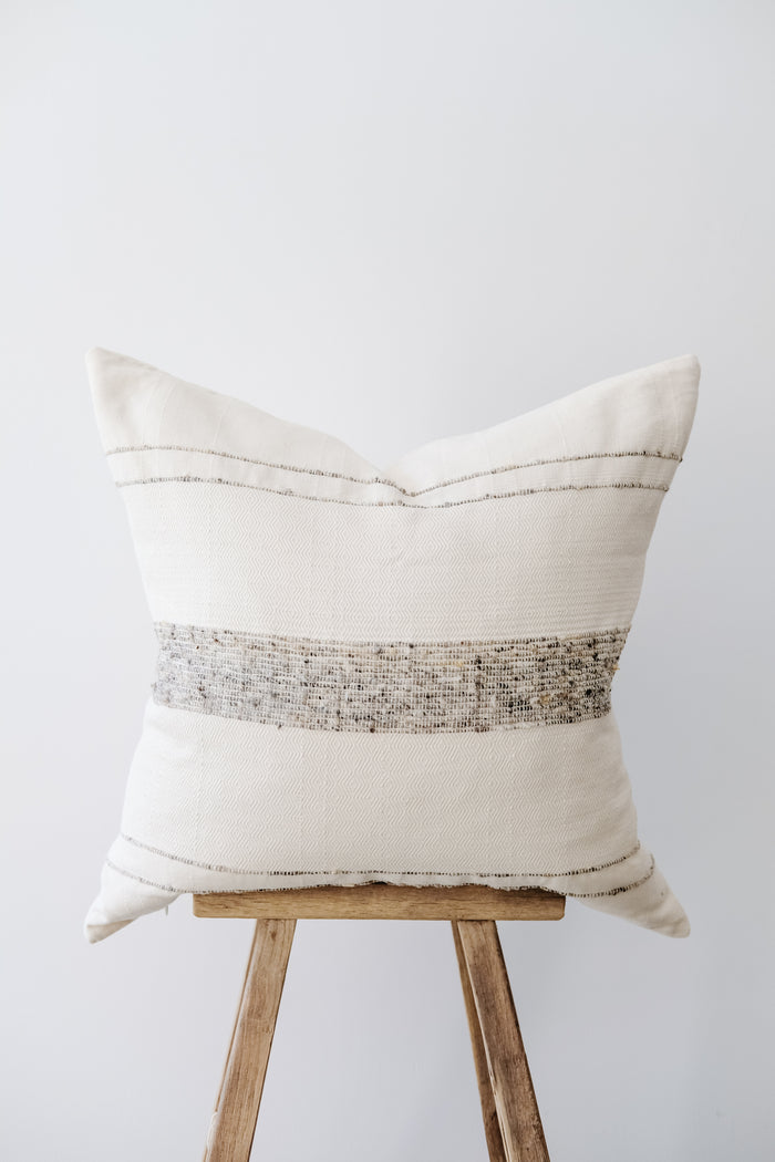 Side view of No. 48 - Azulina - Ivory with Grey Stripe Handwoven Columbian Pillow on a Chinese Stool against a white wall. - Saffron and Poe 