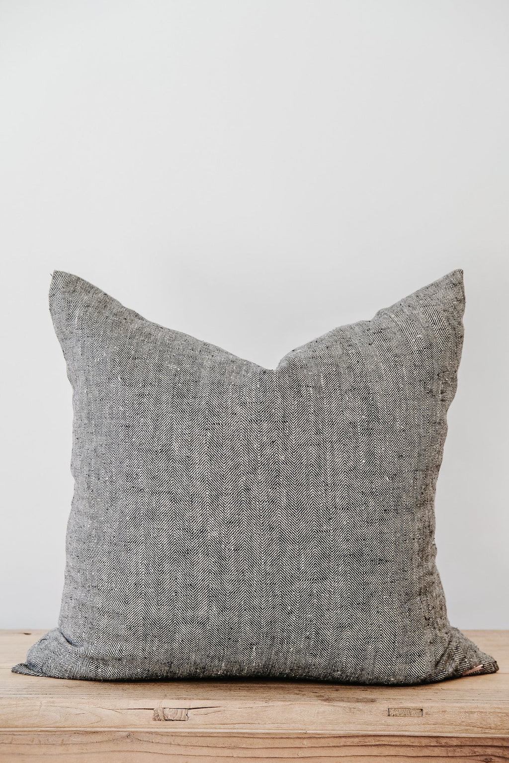 Charcoal chevron linen pillow with textured fabric on wooden surface against white background