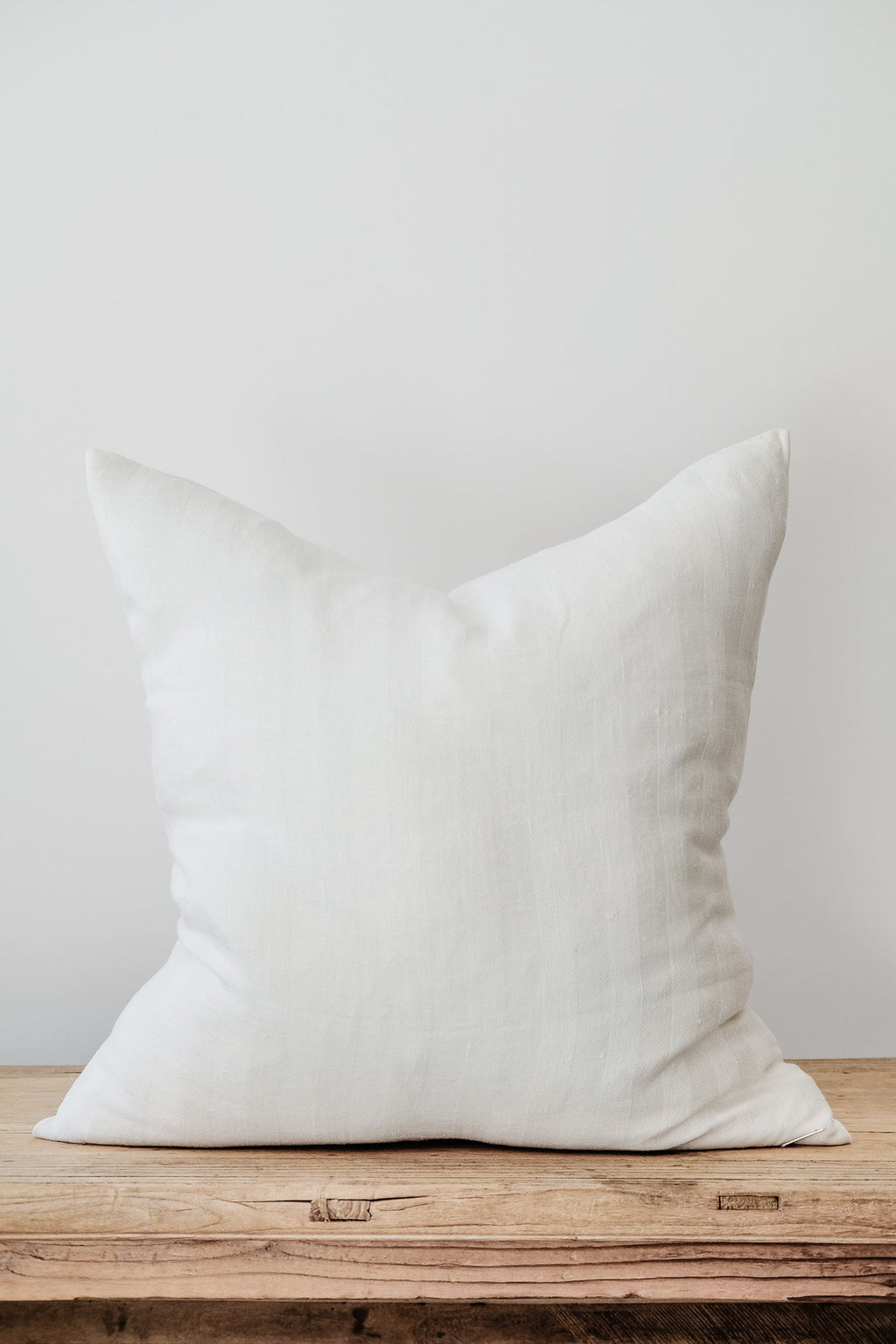 White Chevron linen pillow on wooden surface against plain background