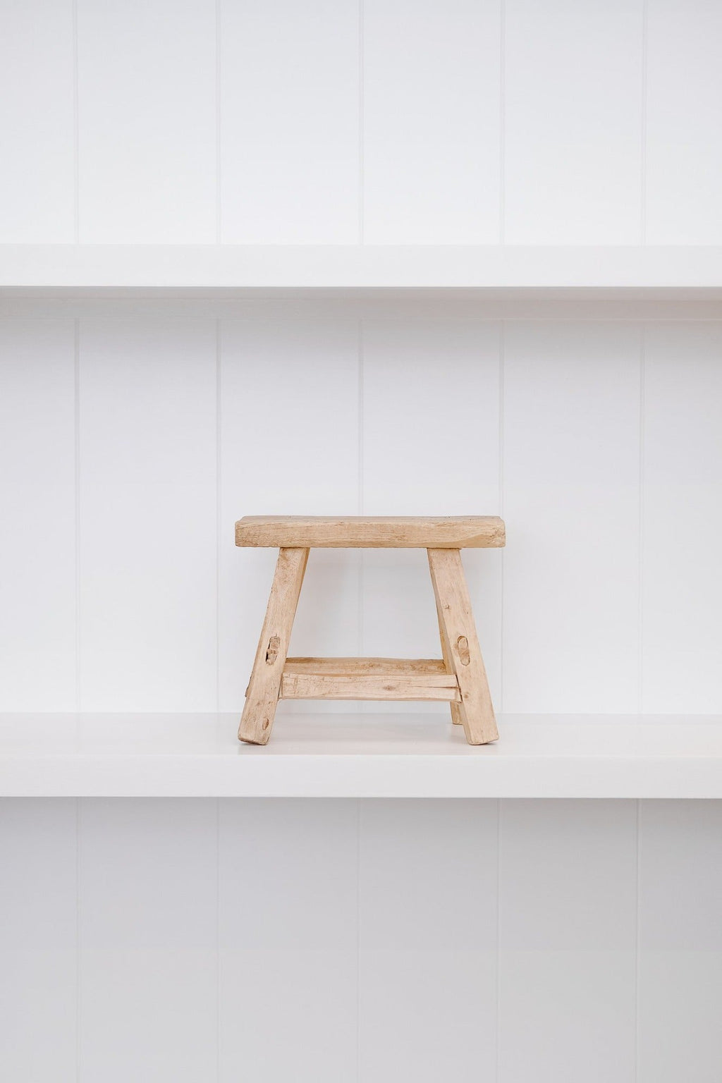 Petite antique elmwood stool with traditional mortise and tenon joinery on white shelf
