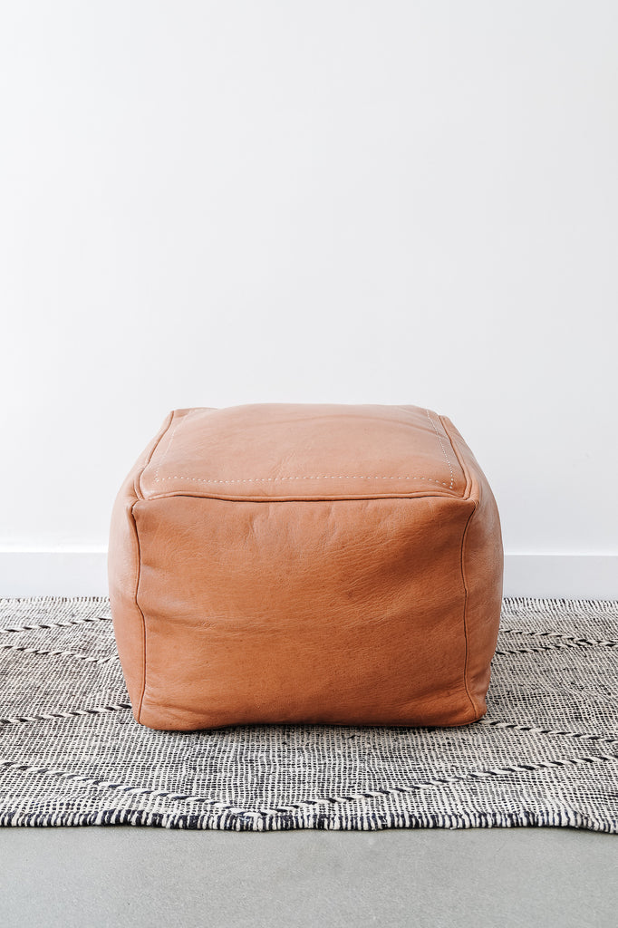 Front view of Square Leather Moroccan Pouf on a Moroccan Kilim Rug against a white wall. - Saffron and Poe