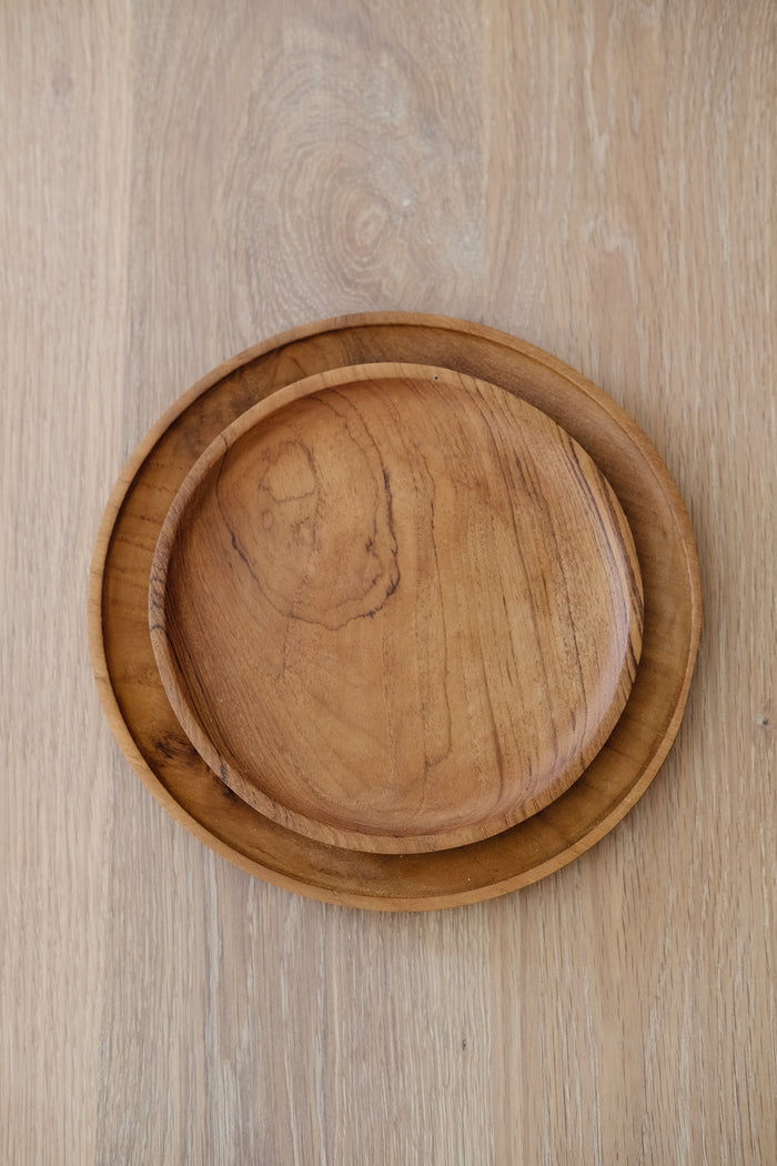 Front view of Teak Plates stacked on an Organic Edge Oak Dining Table. - Saffron and Poe