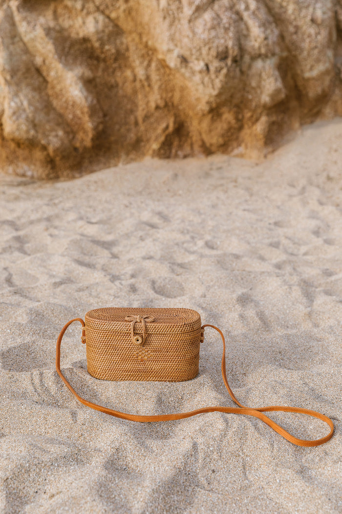 Front view of Tenganan Basket Cross Body - Oval - against a beach background. - Saffron and Poe