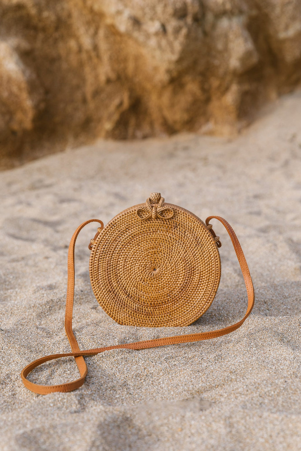Round Tenganan Basket Crossbody bag with leather strap on sandy surface