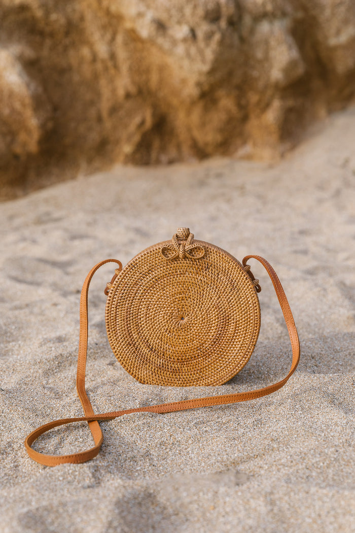 Front view of Tenganan Basket Cross Body - Round - against a beach background. - Saffron and Poe