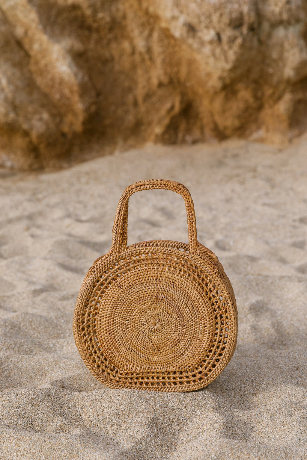 Tenganan Basket Handbag made of natural Ata reed with intricate circular weave standing on sand background
