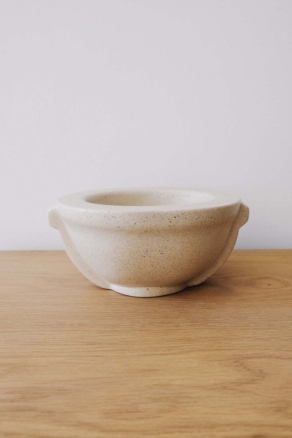 Smooth polished terrazzo vessel on wooden surface against white wall
