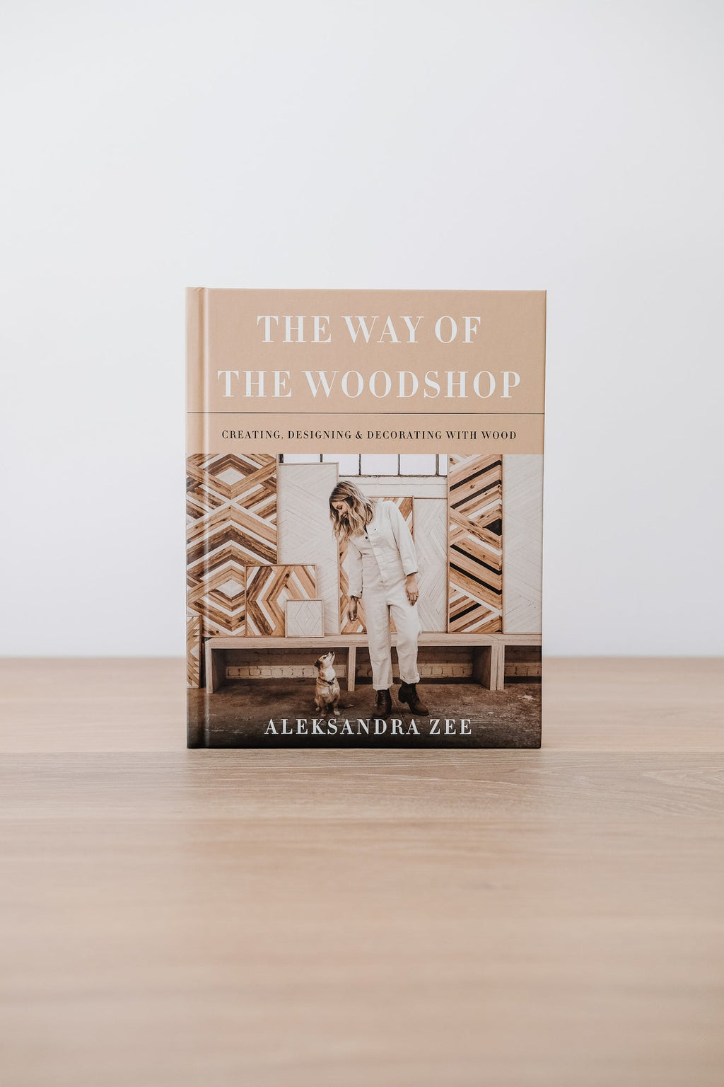 The Way of the Woodshop book by Aleksandra Zee on a wooden surface with wood workshop designs in the background