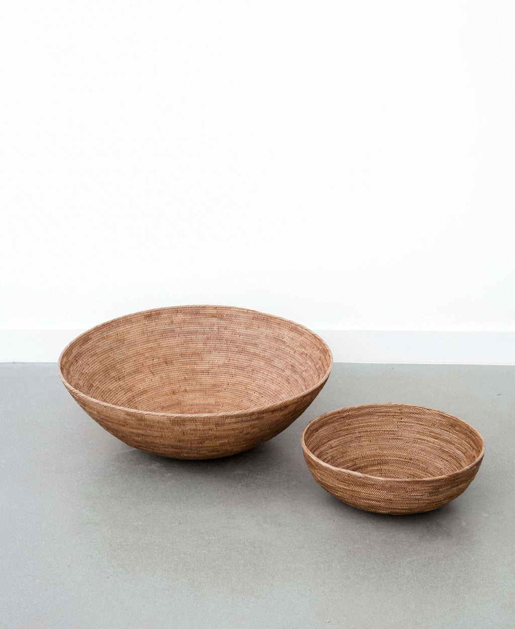 Two handwoven Woven Tenganan Baskets made from natural Ata reed on a gray surface
