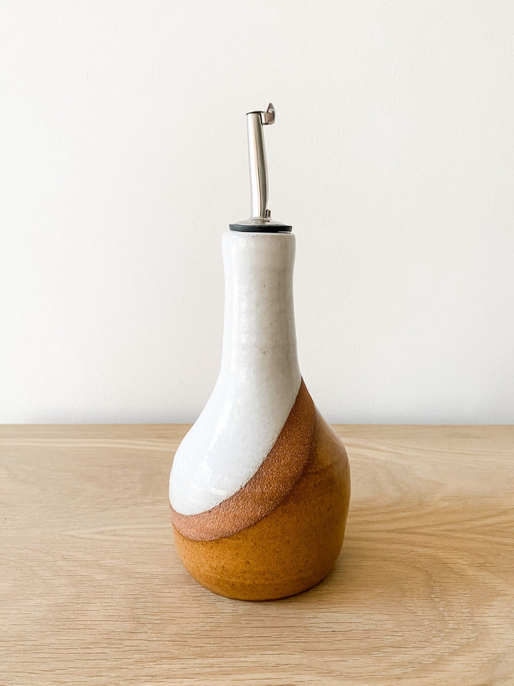 Uzumati Ceramic Olive Oil Bottle with white glaze top and rust glaze base on wooden surface
