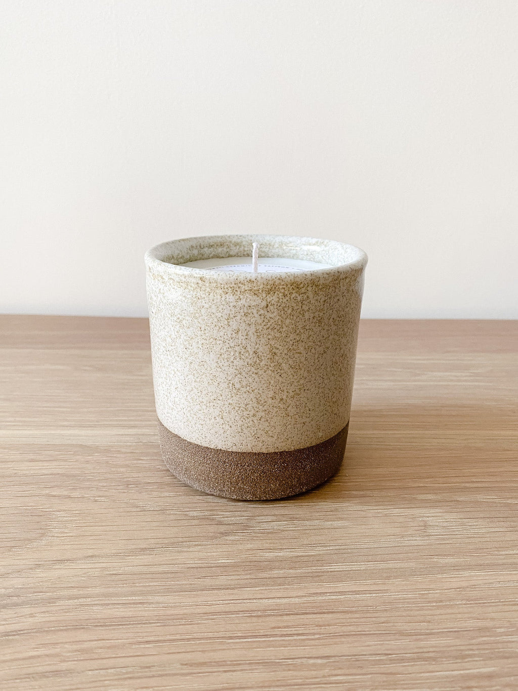 Uzumati Ceramic Coastal Woods Candle in rustic stoneware with speckled white glaze and unglazed deep umber base on wooden surface