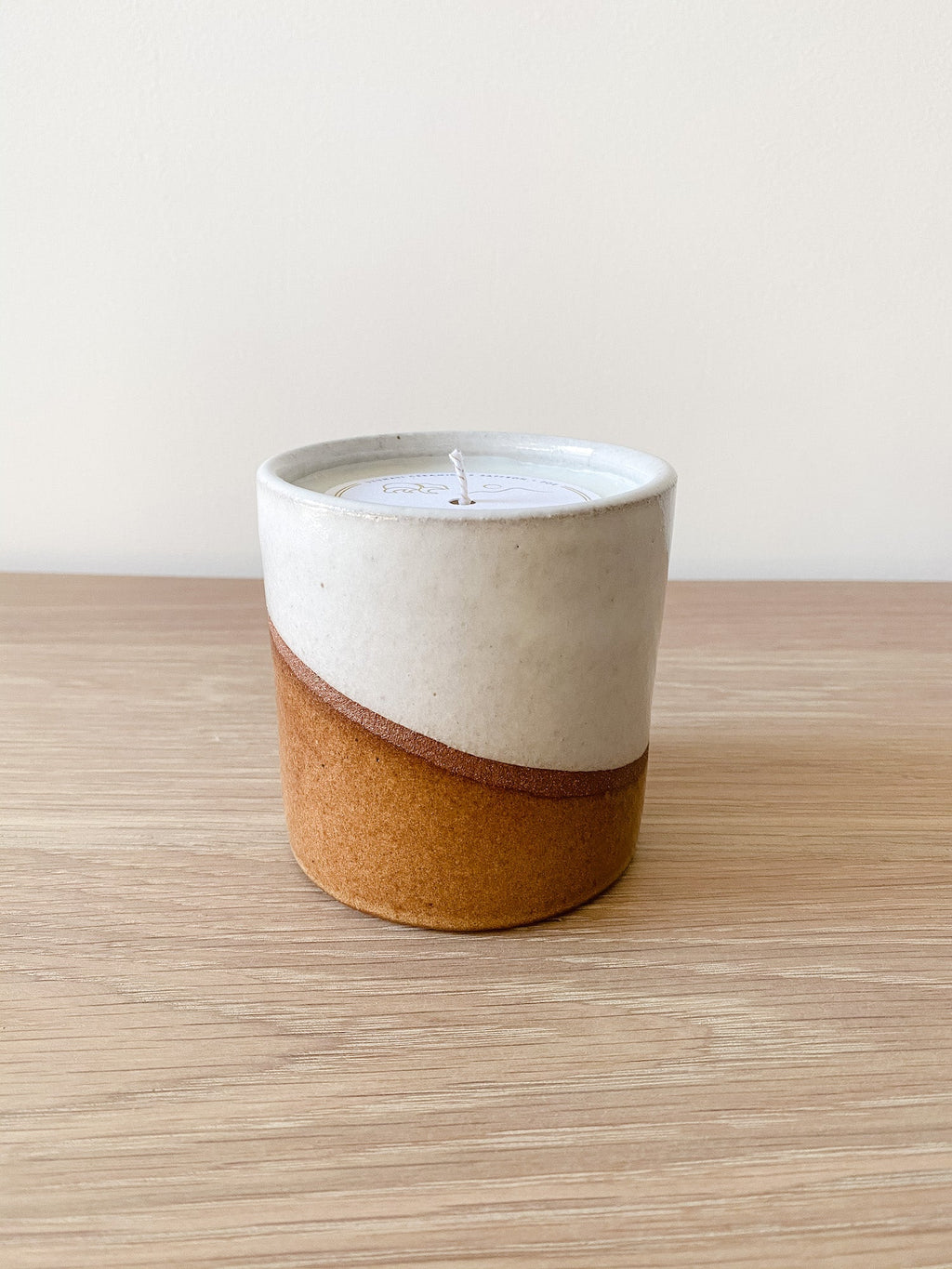 Uzumati Ceramic Desert candle in two-tone stoneware vessel with white glaze top and rust base on wooden surface
