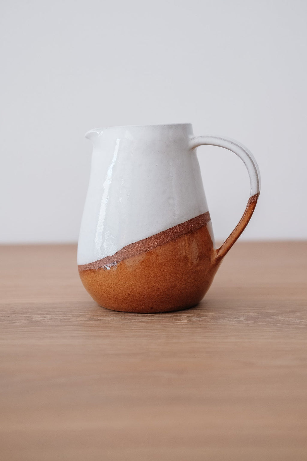 Uzumati Drifter Pitcher with white glaze and rust stoneware on wooden surface