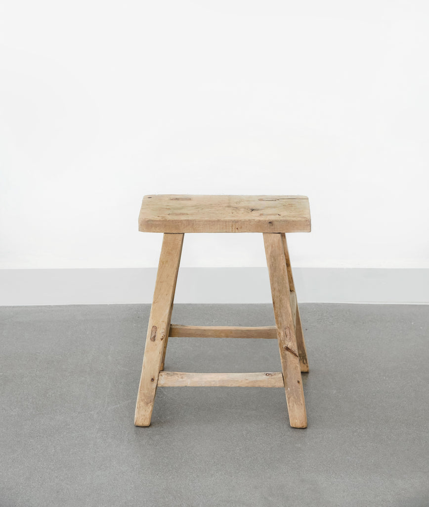 Front view of vintage rectangular stool with concrete flooring and white walls. - Saffron and Poe