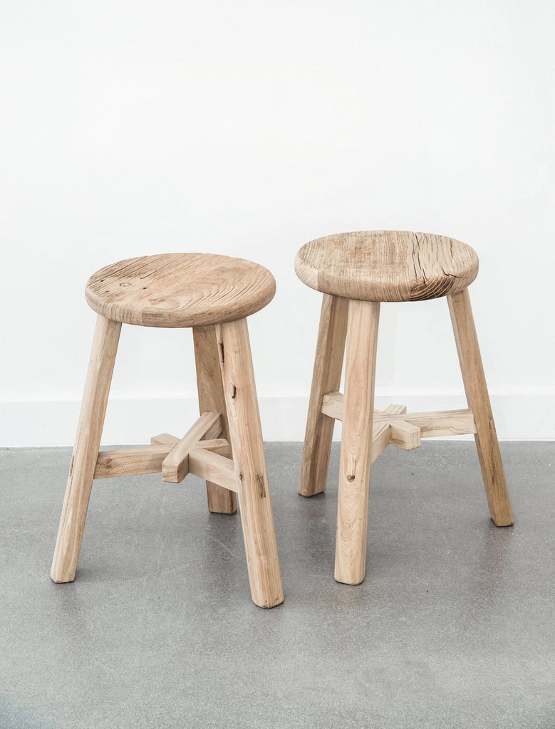 Two vintage round stools against white wall with concrete floor. - Saffron and Poe