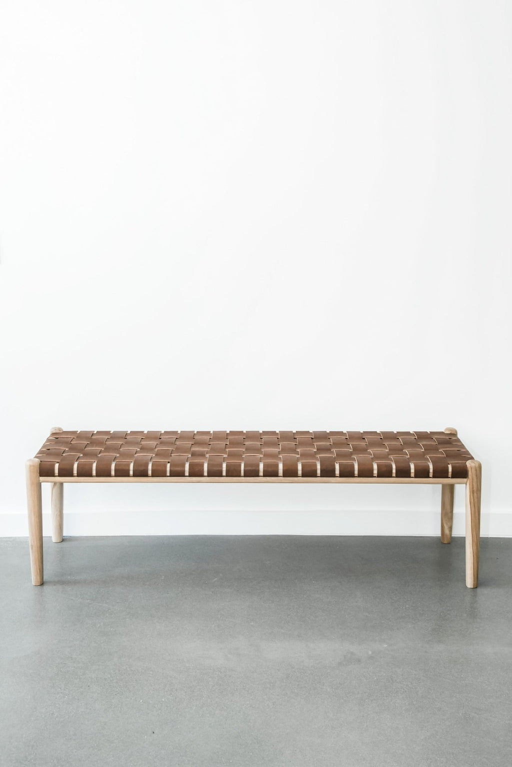 Woven leather bench with teak frame and woven leather seat in saddle color against white wall