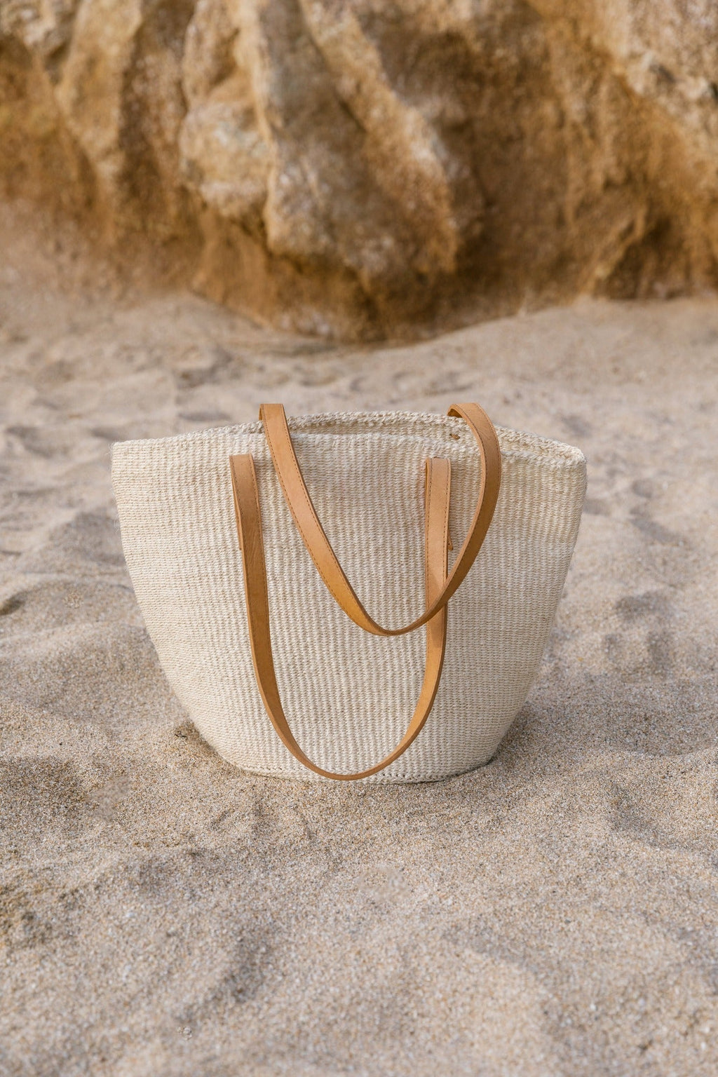 Woven Sisal and Leather Tote bag with cream sisal fiber and leather straps on sandy beach