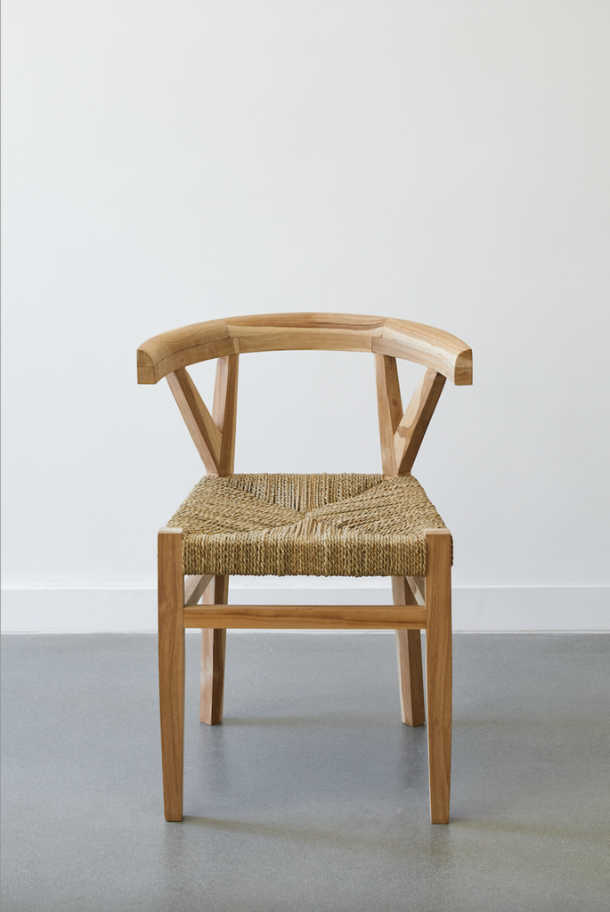 Front view of the Rattan Curved Back Dining Chair against a white background and concrete floors. - Saffron and Poe