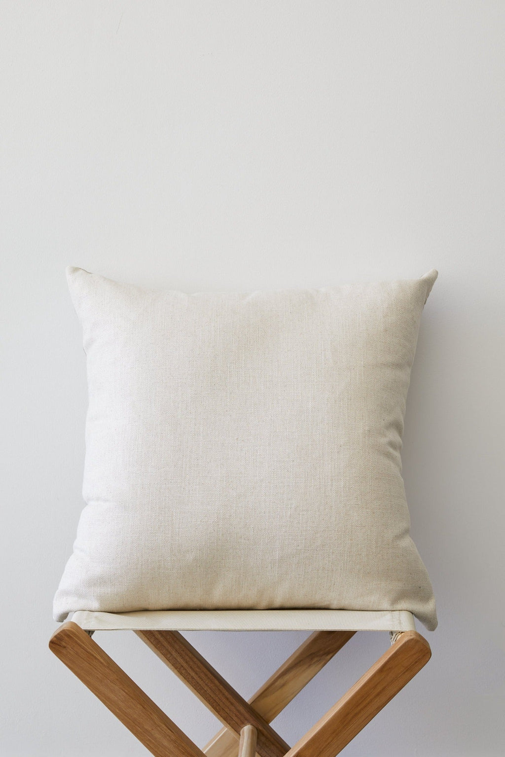 Cream linen chevron pillow on wooden chair against white background