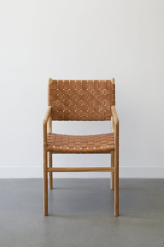 Front view of the Woven Leather Strap Dining Arm Chair in Beige against a white background and concrete floors. -Saffron and Poe