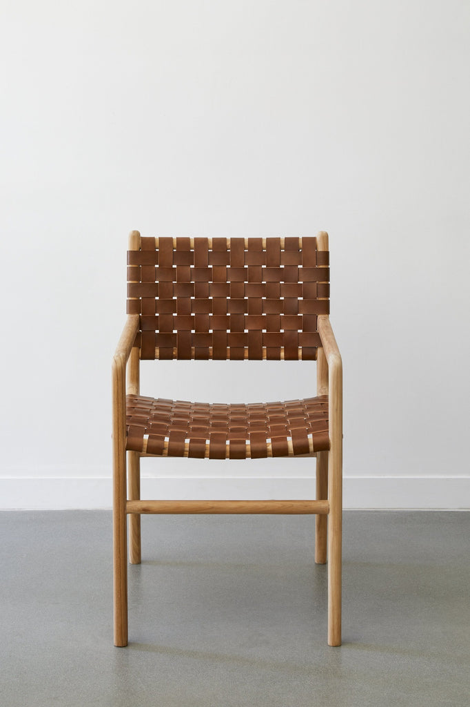 Front view of the Woven Leather Strap Dining Arm Chair in saddle against a white background and concrete floors. - Saffron and Poe