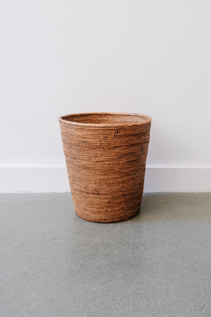 Woven Tenganan waste basket made from natural Ata reed with a tapered shape against a white wall