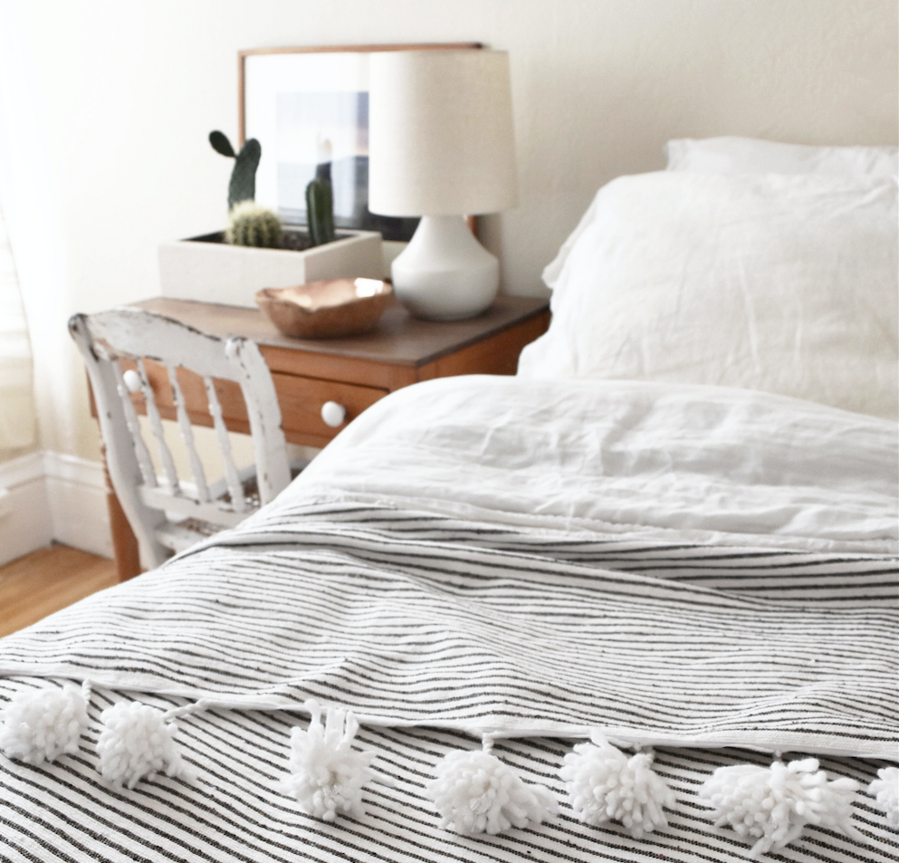 Moroccan Pom Bed Throw in dark grey and white stripes with oversized white pom tassels on a bed
