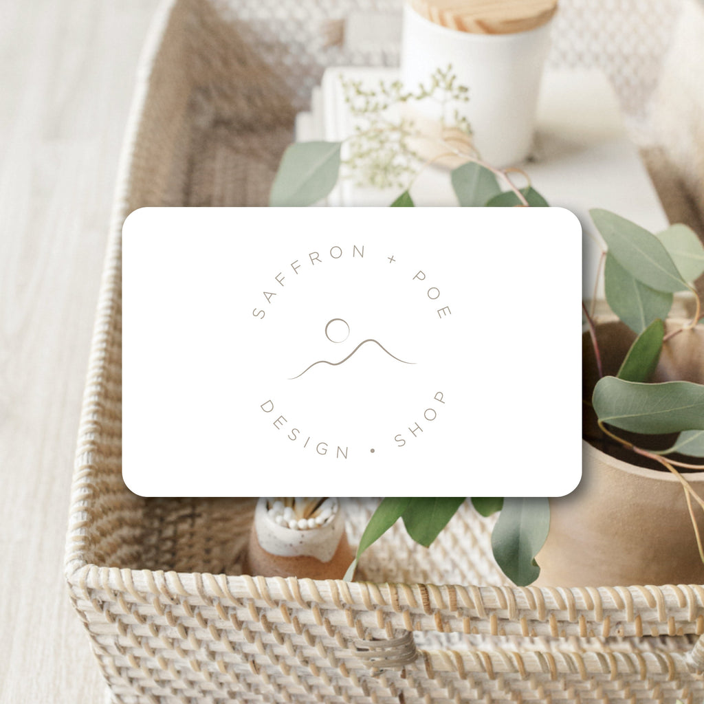 Saffron + Poe gift card on woven basket with greenery and decorative items.