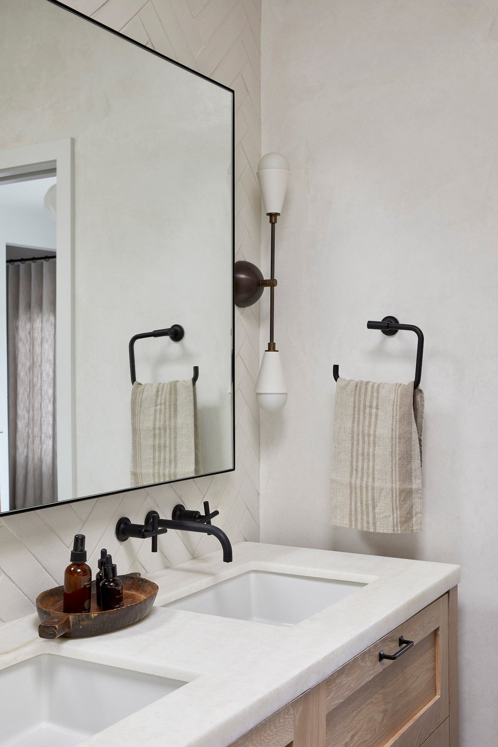 Natural stripe linen hand towels hanging on black towel holder in modern bathroom with double sink and large mirror