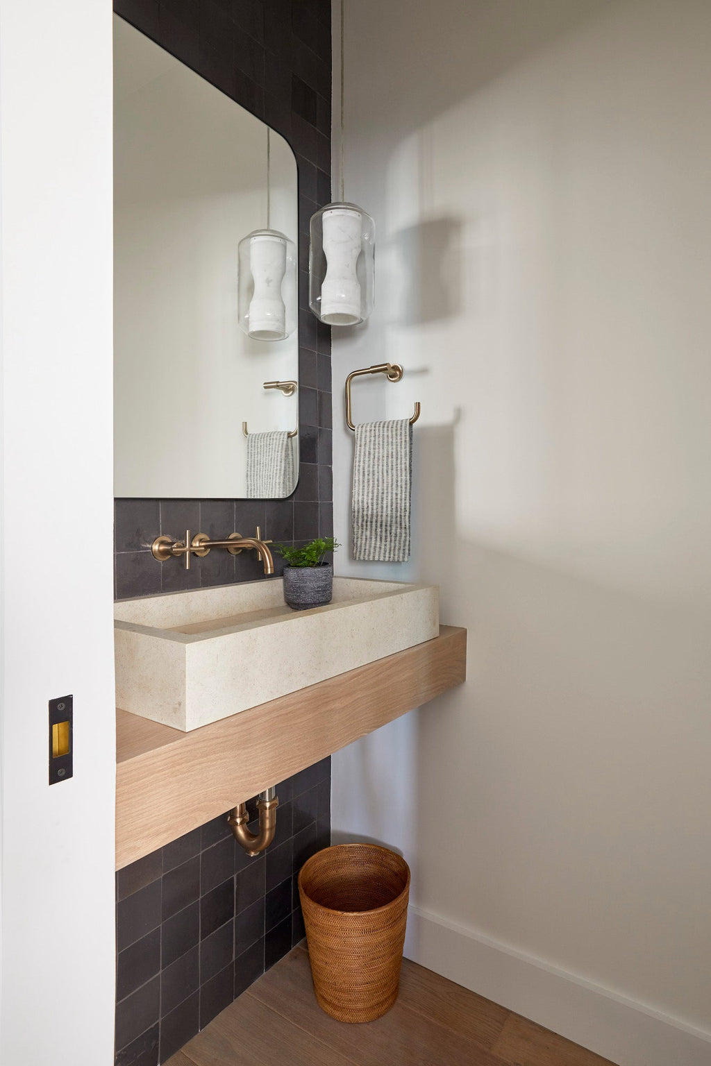 Woven Tenganan waste basket placed under a modern bathroom sink with wooden countertop and black tile wall