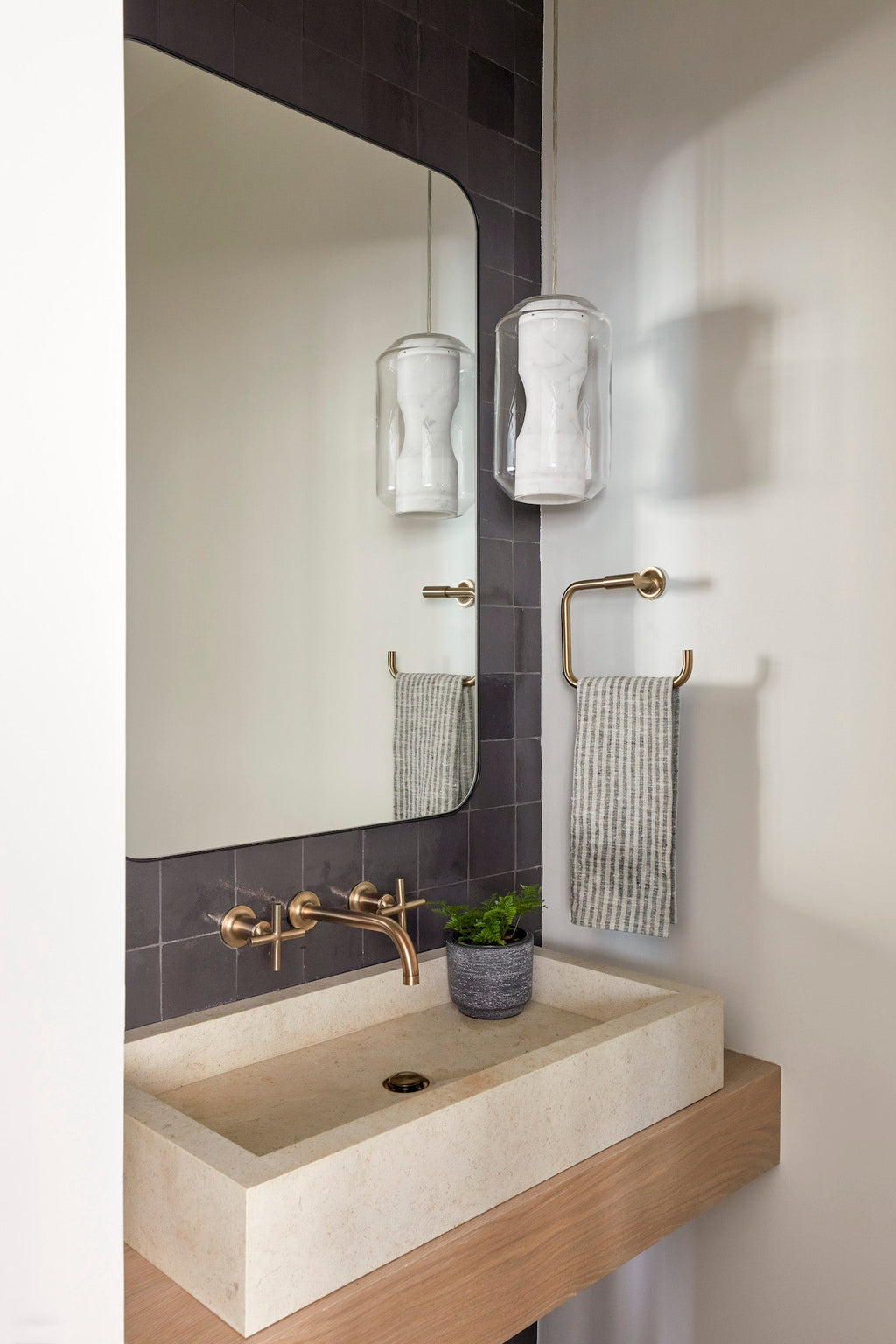 Small stripe linen hand towels hanging on brass towel rack in modern bathroom with stone sink and dark tile wall