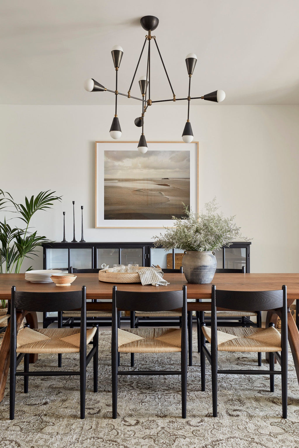 Modern dining room with wooden table, black chairs, abstract chandelier, and decorative plants