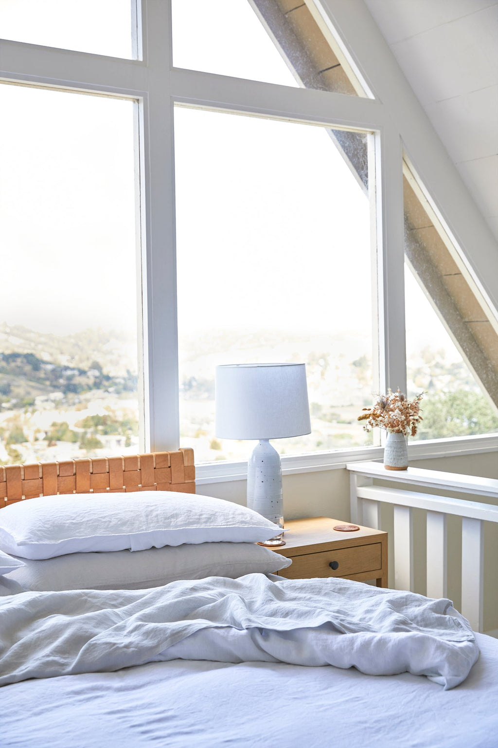 white linen duvet set on bed in bright room with large windows and wooden nightstand