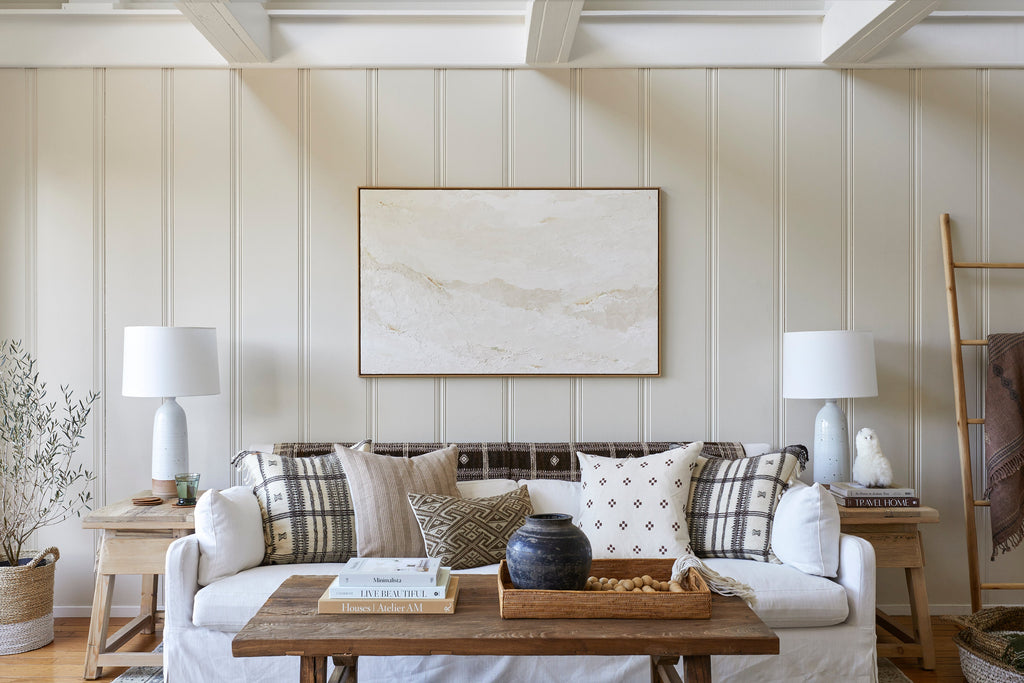 Antique clay pot with dark patina on wooden tray in cozy living room with neutral tones and textured pillows