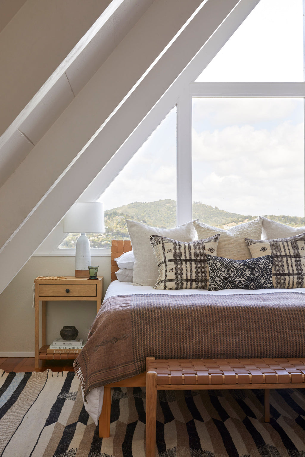 Cozy bedroom featuring white linen duvet set with stylish pillows and wooden furniture under slanted ceiling.