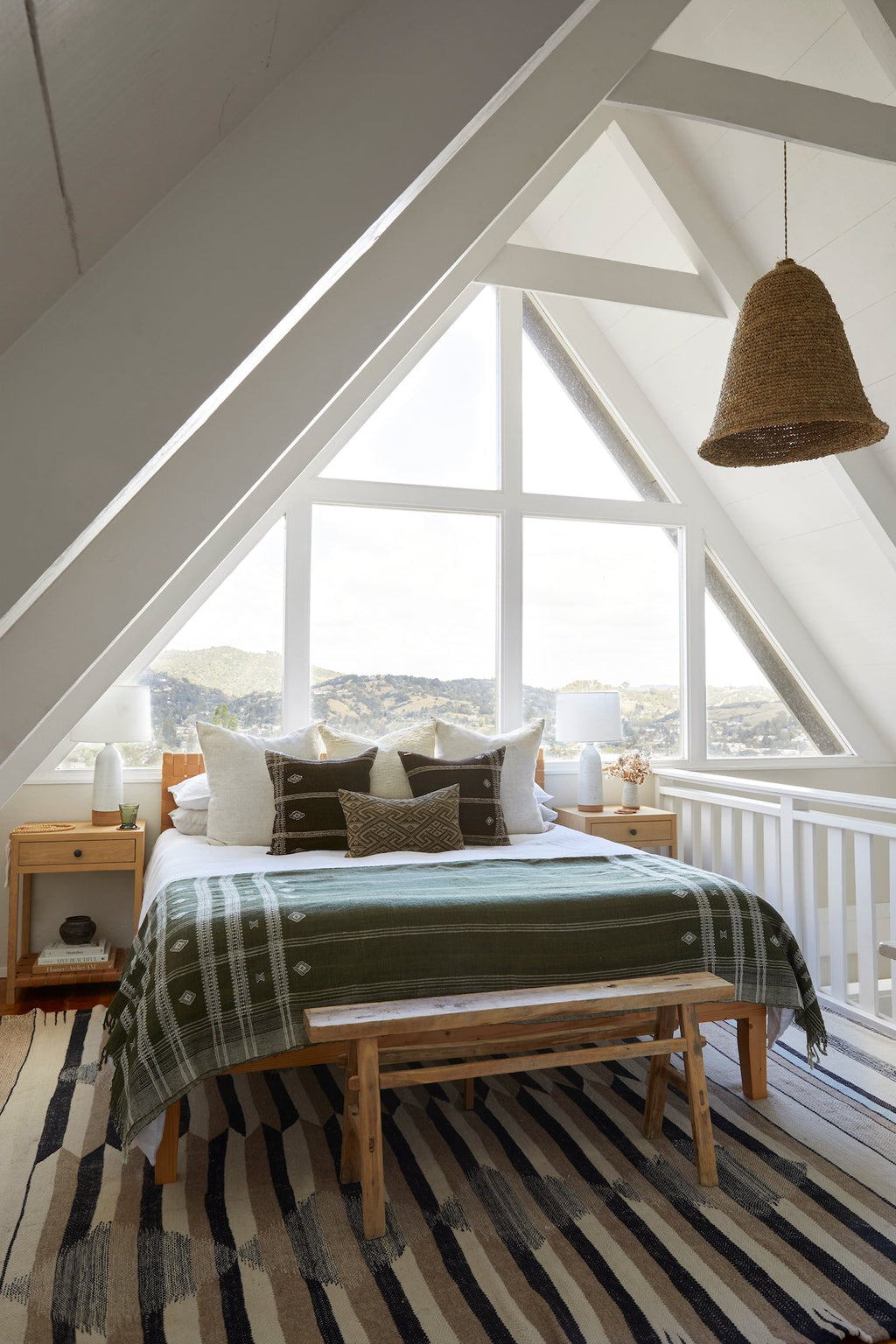 Handwoven Bhujodi Blanket in olive draped over bed in bright attic bedroom with wooden bench and striped rug