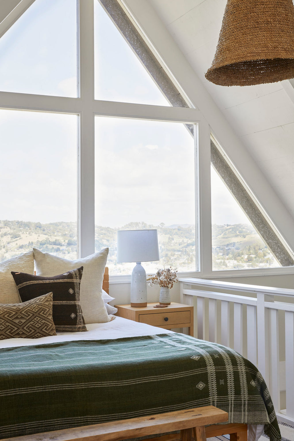 Handwoven Bhujodi Blanket in olive draped on bed in bright attic bedroom with large windows and neutral decor