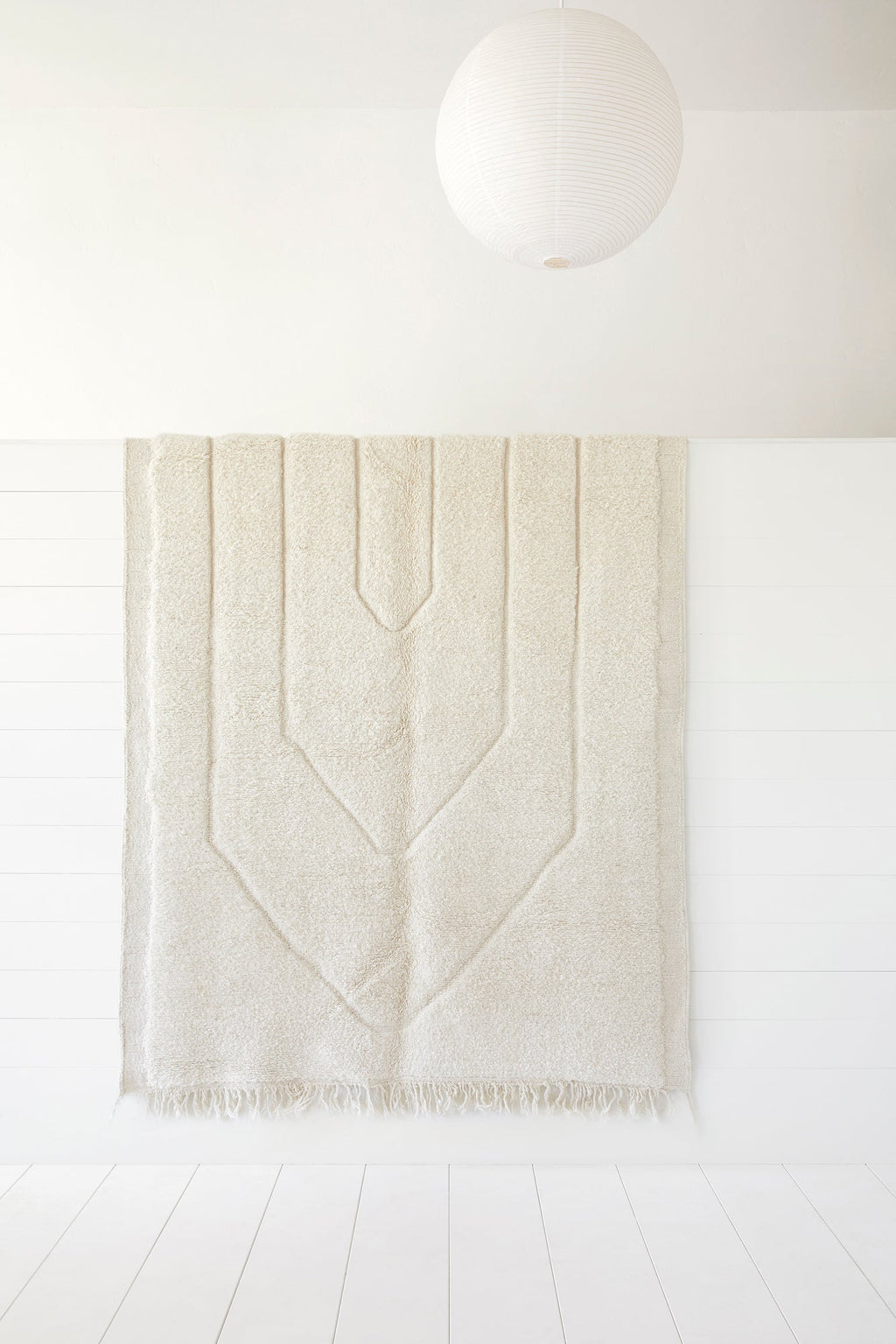 No. 19 - Beni Ourain Rug with neutral geometric pattern hanging on white wall under round paper lantern