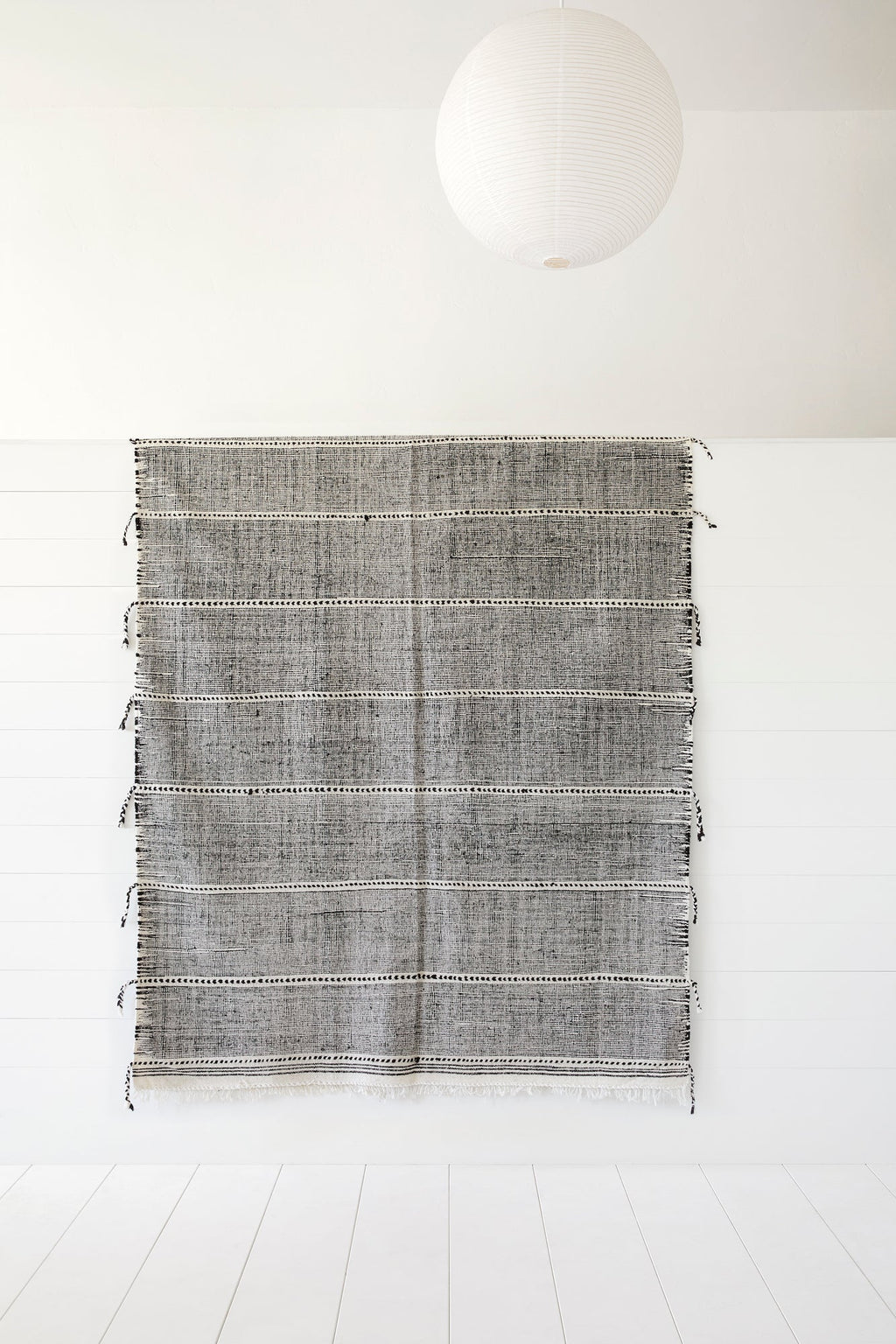 Moroccan flat weave Kilim rug with geometric patterns and fringe hanging on white wall